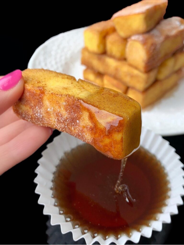 a keto french toast stick being dipped into sugar free maple syrup