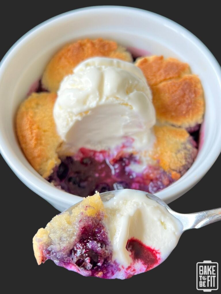 keto blueberry cobbler with a spoonful taken out and shown on the spoon. topped with vanilla ice cream