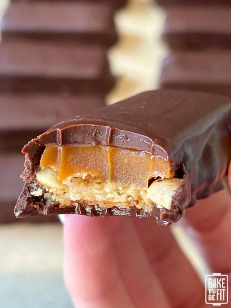 a hand holding a keto snickers bar with a bite taken out