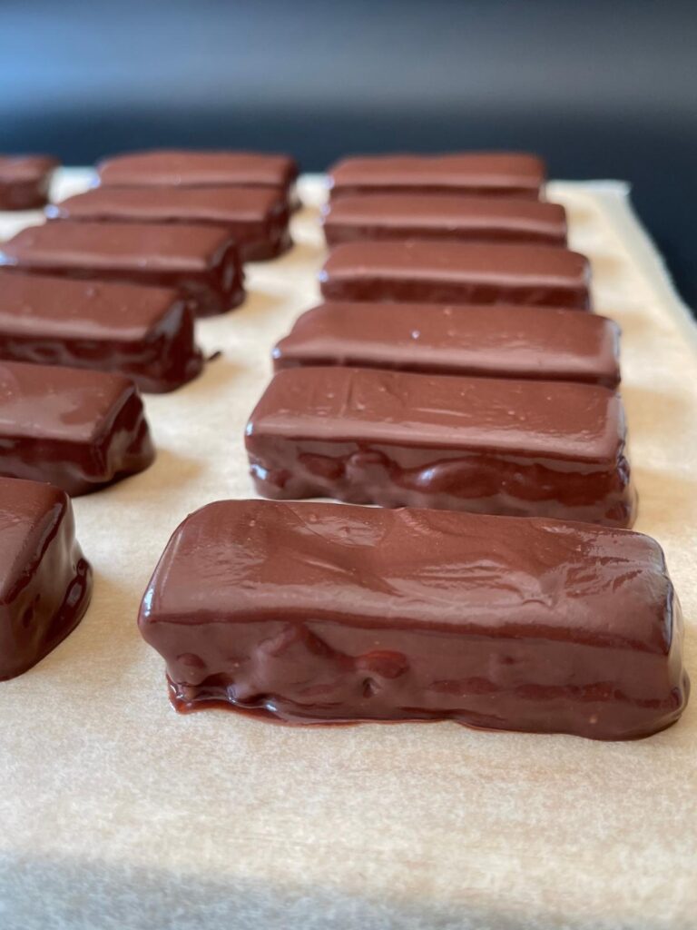 the snickers bars after being dipped in chocolate, on a piece of parchment paper to set