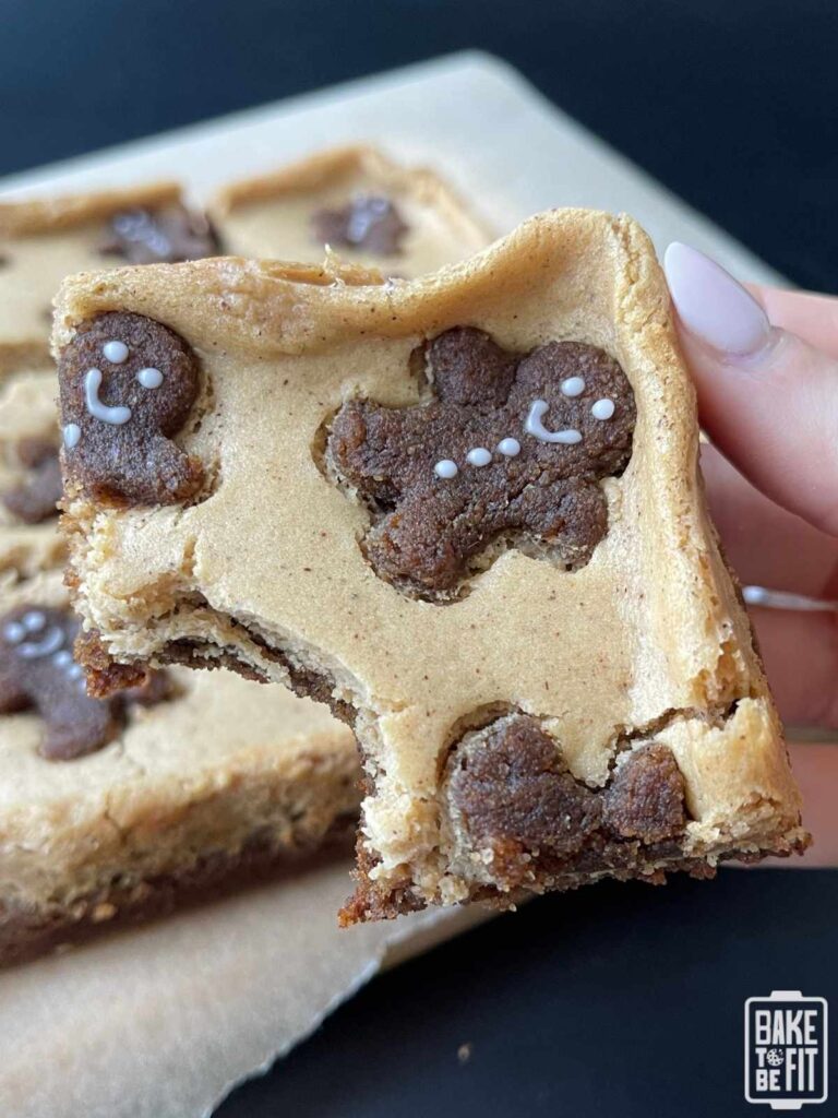 a hand holding a keto gingerbread cheesecake bar with a bite taken out